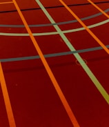 A sports court with intersecting lines in orange and blue, creating geometric patterns on a reddish-brown surface.