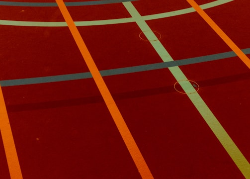 A sports court with intersecting lines in orange and blue, creating geometric patterns on a reddish-brown surface.