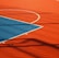 A vibrant sports court with sections of red and blue, featuring crisp white lines marking the boundaries. Shadows from a structure create geometric patterns across the surface, adding depth and interest to the scene.
